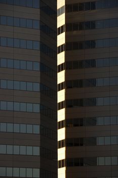 Side exterior of urban skyscraper building with light reflecting off windows.