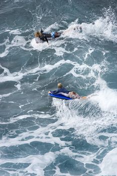 Two adolescent Caucasian males riding boogie boards on wave in Maui.