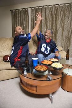 African-American father and son giving high five while watching football game.