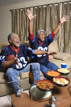Middle-aged African-American couple cheering and watching football game.