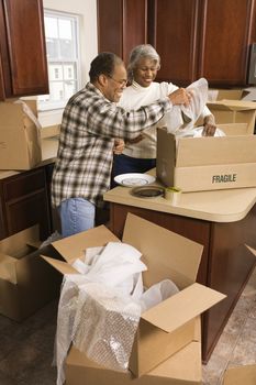 Middle-aged African-American couple packing moving boxes in kitchen.