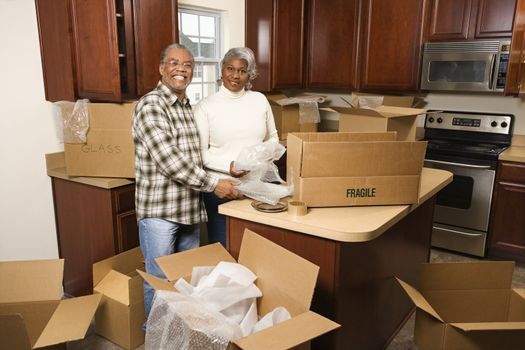 Portrait of middle-aged African-American couple packing moving boxes in kitchen.