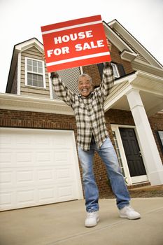 Portrait of middle-aged African-American male outside house holding up for sale sign.