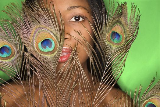 African-American mid-adult woman looking through peacock feather.