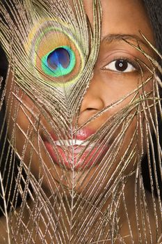 Close-up smiling African-American mid-adult woman looking through peacock feather.