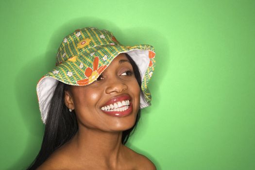 Smiling African-American mid-adult woman wearing green hat on green background.