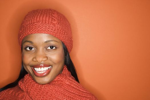 African-American mid-adult woman wearing orange scarf and hat on orange background.