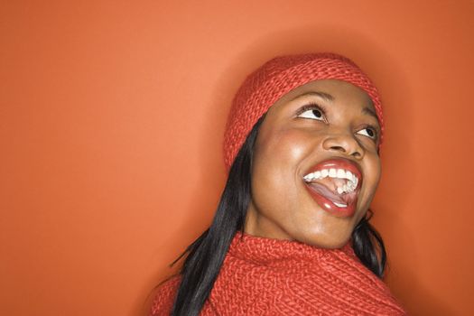 Laughing African-American mid-adult woman wearing orange scarf and hat on orange background.