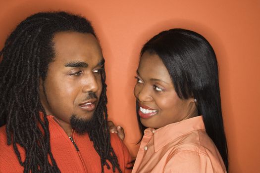 African-American mid-adult couple wearing orange clothing on orange background.