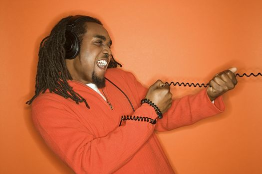 African-American mid-adult man pulling on cord wearing headphones and orange clothing on orange background.