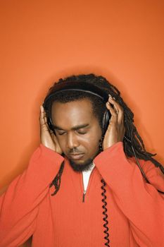 African-American mid-adult listening to headphones wearing orange clothing on orange background.