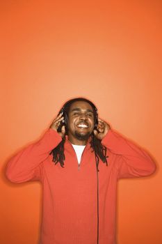 African-American mid-adult man listening to headphones wearing orange clothing on orange background.