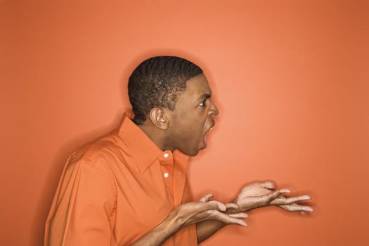 Side view of young African-American man on orange background expressing anger towards unseen person.