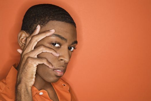 Young African-American man with hand on his face on orange background.