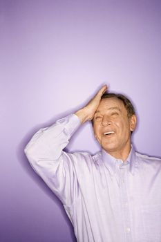 Smiling middle-aged Caucasian man on purple background with his hand on his forehead.