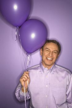 Smiling middle-aged Caucasian man on purple background holding purple balloons.