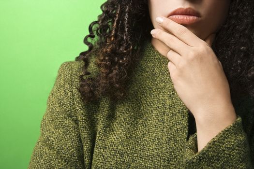 Close-up of young Caucasian woman with hand on chin on green background wearing green clothing.