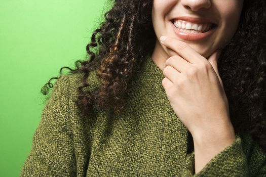 Close-up of smiling young Caucasian woman with hand on chin on green background wearing green clothing.