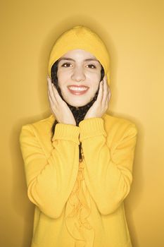 Smiling young Caucasian woman wearing yellow raincoat on yellow background.