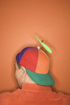 Back view of middle-aged Caucasian man wearing propeller cap on orange background.