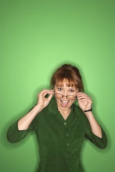 Smiling Caucasian mid-adult woman putting on eyeglasses, on green background.