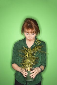 Caucasian mid-adult woman on green background looking at plant.