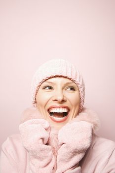 Smiling Caucasian mid-adult woman on pink background wearing winter coat and hat.