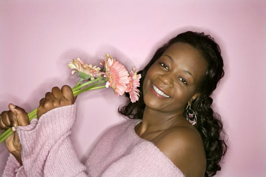 Portrait of smiling African-American mid-adult woman on pink background holding pink flowers.
