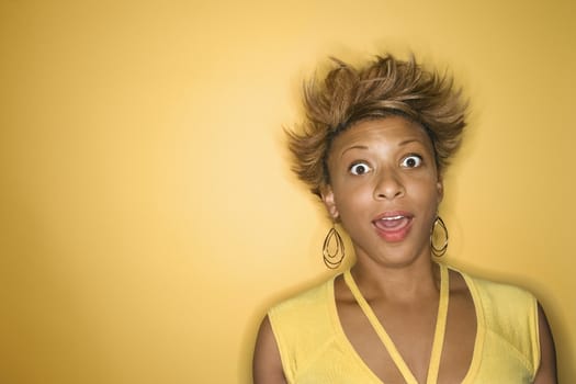 Portrait of surprised African-American young adult woman on yellow background.