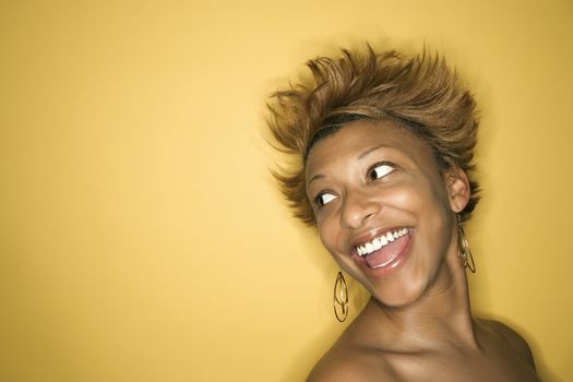 Portrait of smiling African-American young adult woman on yellow background.