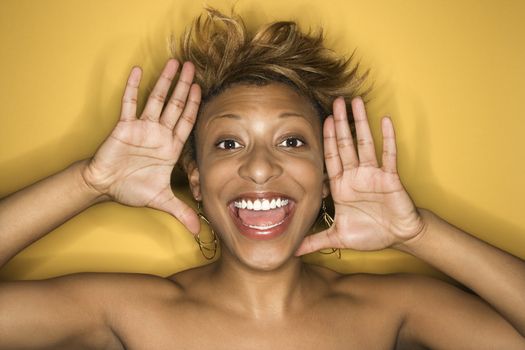 Portrait of young African-American adult woman on yellow background yelling at the viewer.