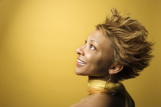 Side view portrait of smiling young African-American adult woman on yellow background.