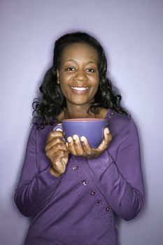 Portrait of smiling mid-adult African-American woman on purple background holding latte cup.