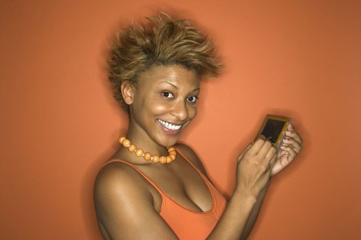 Portrait of smiling young African-American adult woman on orange background using her palmtop computer.