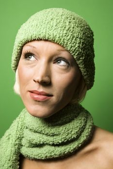 Head and shoulder portrait of smiling young adult Caucasian woman on green background wearing winter hat and scarf.