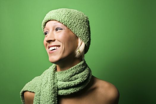 Portrait of smiling young adult Caucasian woman on green background wearing winter hat and scarf.