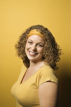 Portrait of smiling young adult Caucasian woman on yellow background.