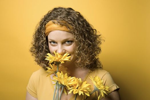Portrait of young adult Caucasian woman on yellow background holding and smelling bouquet of flowers.