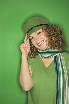 Portrait of smiling young adult Caucasian woman on green background wearing hat and scarf.