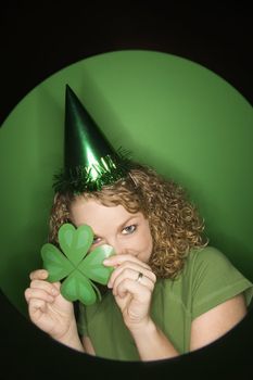 Vignette of young adult Caucasian woman on green background wearing Saint Patricks Day hat and holding shamrock.