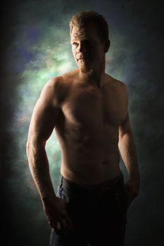 Dramatically lit portrait of shirtless young adult Caucasian man on studio background.