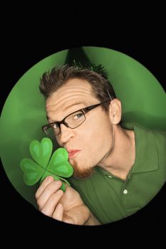 Vignette of adult Caucasian man on green background wearing Saint Patricks Day hat and kissing shamrock.