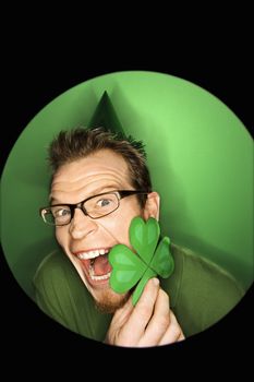 Vignette of excited adult Caucasian man on green background wearing Saint Patricks Day hat and holding shamrock.
