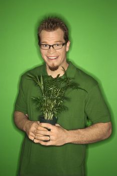 Portrait of smiling adult Caucasian man on green background holding plant.