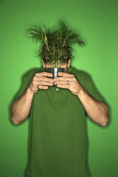 Portrait of adult Caucasian man on green background holding plant in front of his face.