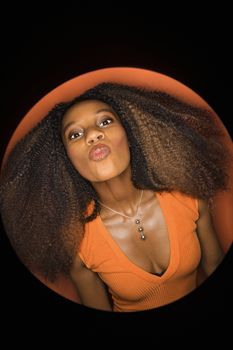 Vignette of young African-American adult woman with big hair and low cut dress on orange background puckering her lips.
