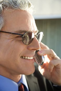 Close up profile of prime adult Caucasian man in suit smiling and talking on cellphone in urban setting.