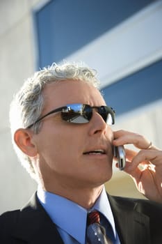 Close up side view of prime adult Caucasian man in suit talking on cellphone in urban setting.