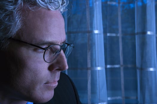 Blue tone close up profile of prime adult Caucasian man in suit.