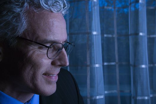 Blue tone close up profile of prime adult Caucasian man in suit smiling.